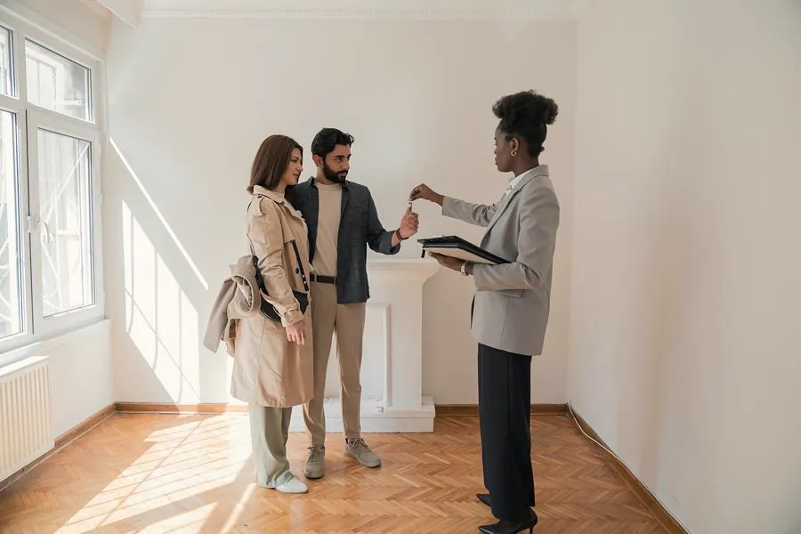 An agent hands a couple the keys in a bright, empty flat with a parquet floor.
