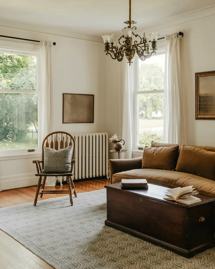 A bright, furnished living room with a chandelier, a leather sofa and windows onto a garden.
