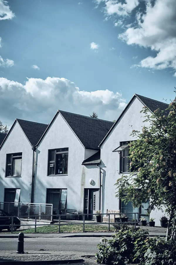 Three white gabled houses side by side under a blue sky with clouds.