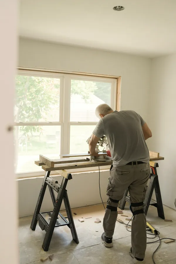 A builder cutting timber on trestles in a bare, bright room.