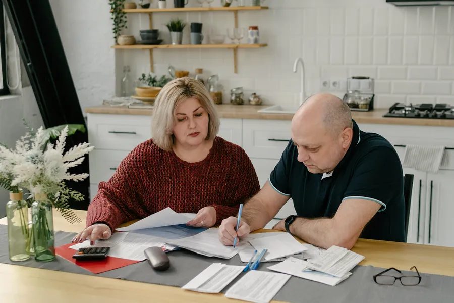A woman and a man going through papers and a calculator at their kitchen table.